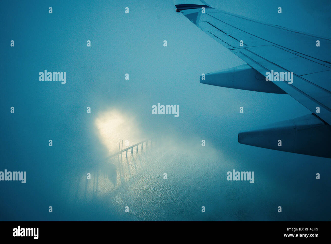Flugzeugflügel durch Wolken Fliegen über Wasser Stockfoto