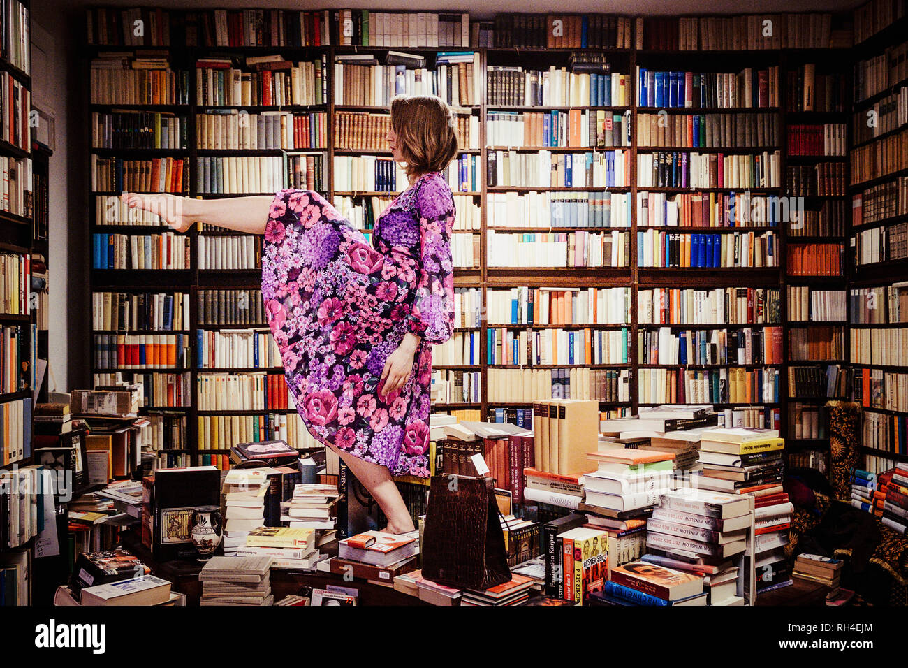 Überschwängliche Frau, die in der Bibliothek auf Bücherstapeln tanzt Stockfoto