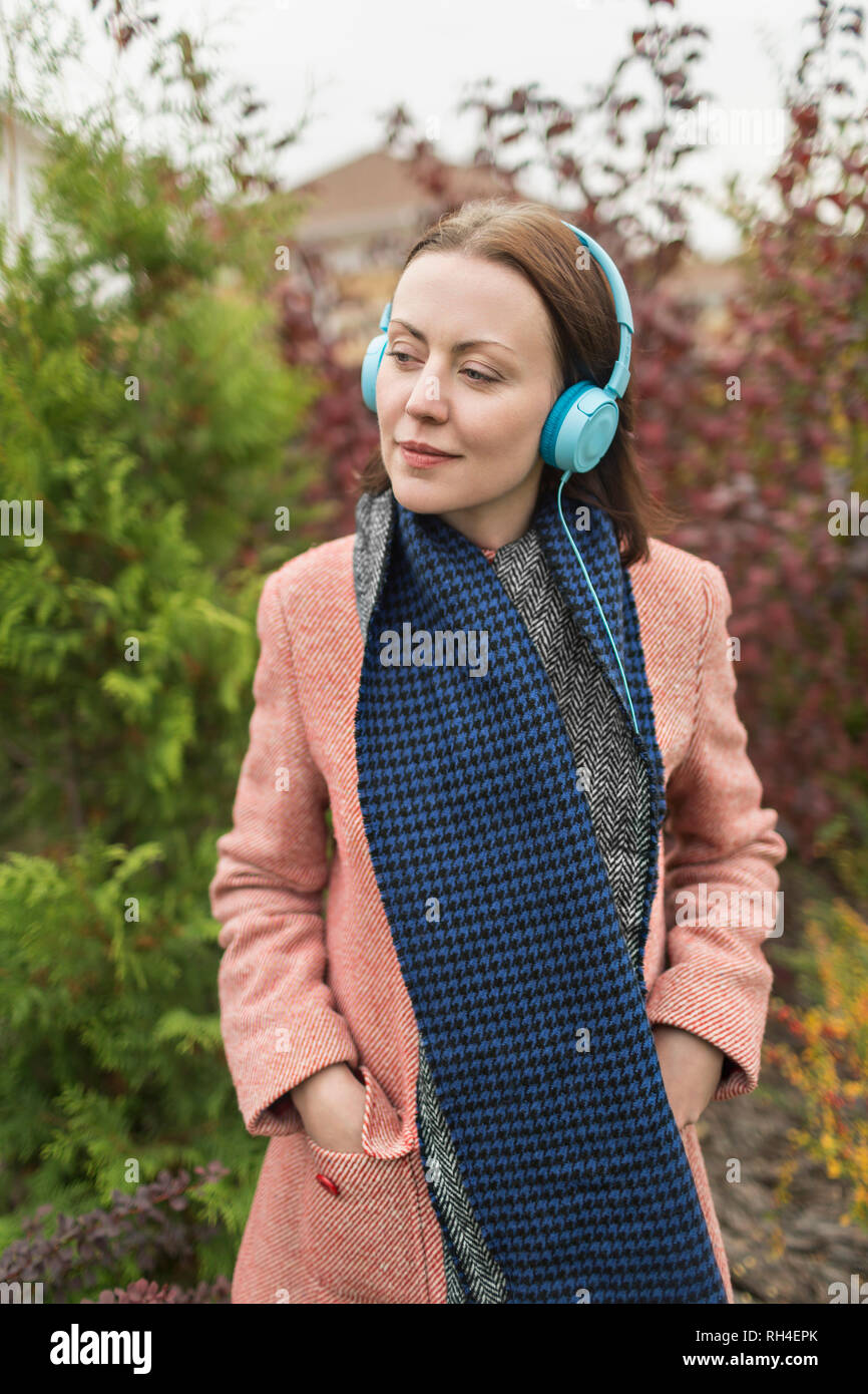 Frau in Schal und Mantel Musikhören mit Kopfhörern Stockfoto