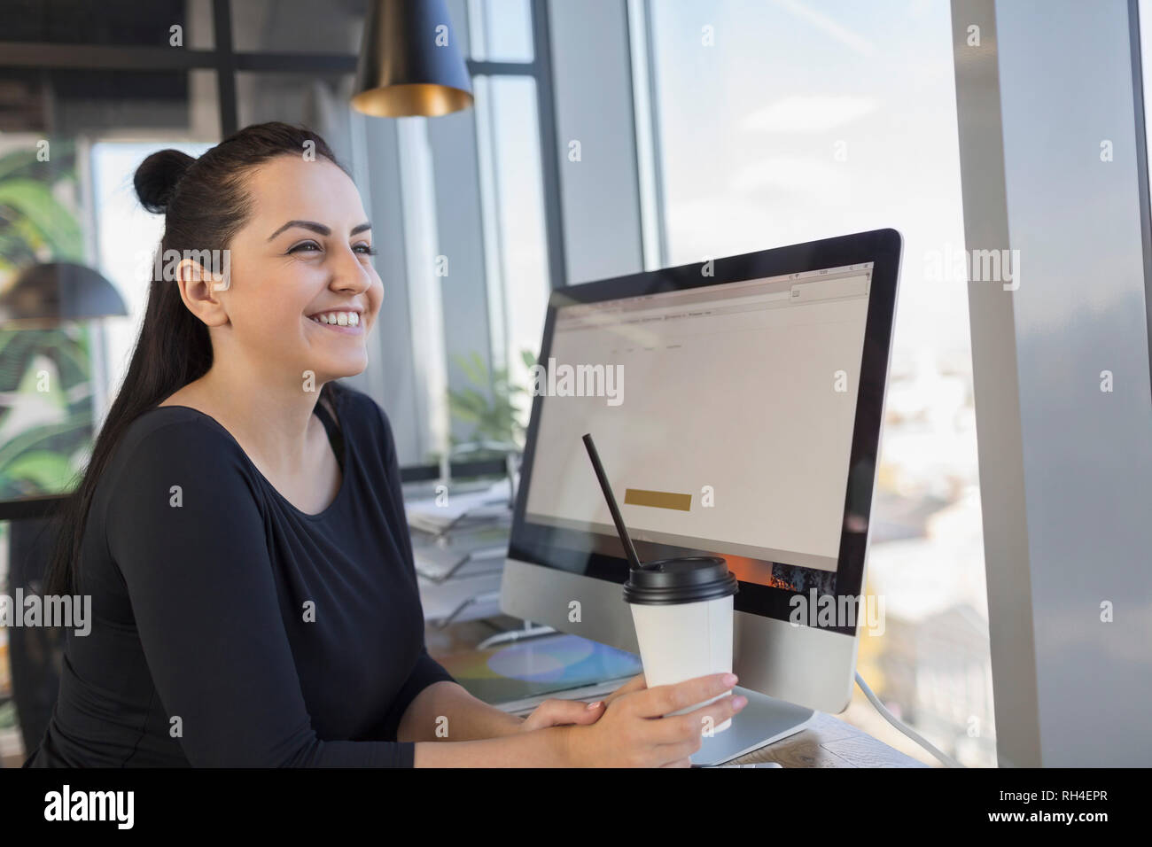 Lächelnde Frau trinkt Kaffee und benutzt einen Computer im Internetcafe Stockfoto