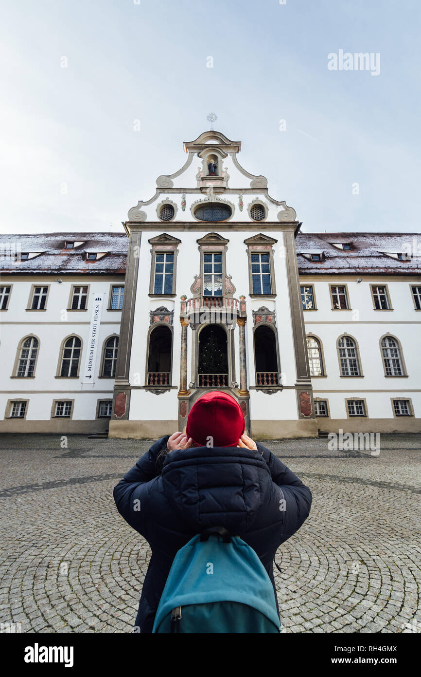 Füssen, Deutschland - Dezember 2018: die Frau in Rot hat im Hinterhof des Benediktinerklosters St. Mang. Vertikale Ausrichtung. Stockfoto