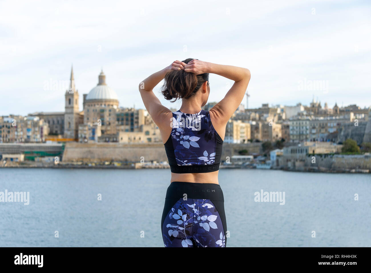 Rückansicht einer Frau, die ihre Haare einstellen, bevor Sie draussen trainieren. Valletta Malta Hintergrund. Stockfoto