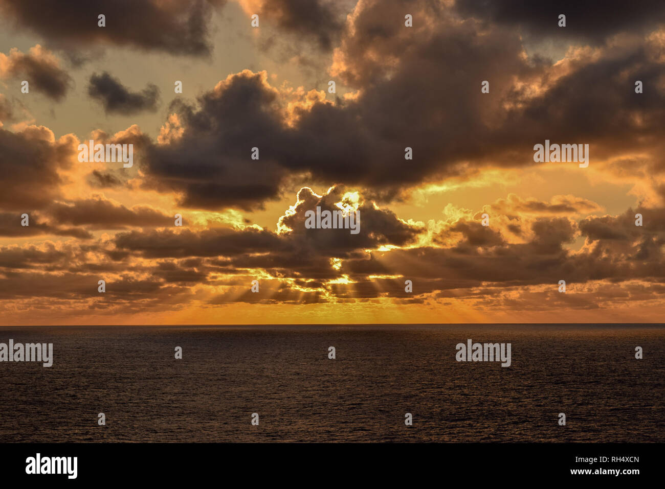 Herrliche orange leuchtende Himmel als Sonnenstrahlen über dem Horizont, verteilt kurz vor Sonnenuntergang über dem karibischen Meer an einem bewölkten Abend. Stockfoto