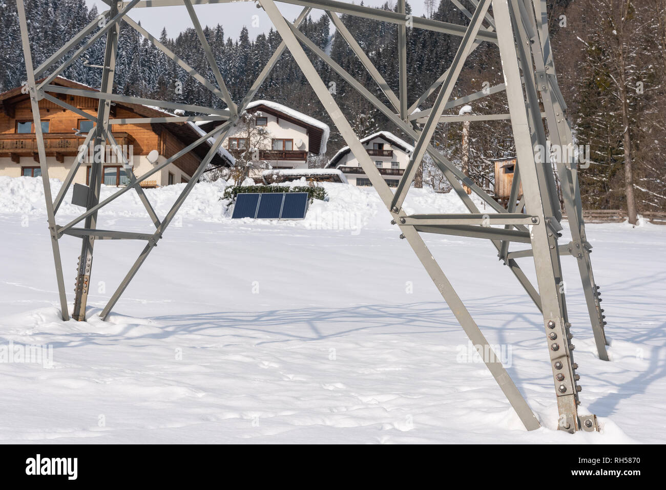 Häuser mit Solar PV Panels durch eine hohe Spannung Strommast gesehen. Einen sonnigen Tag und alles mit Schnee bedeckt. Stockfoto