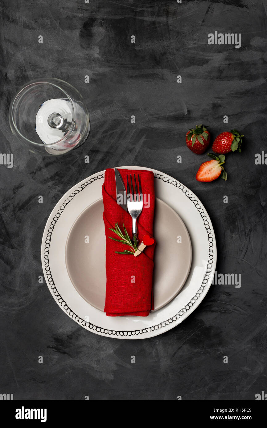 Valentines Tag, Tisch und romantisches Abendessen Konzept - Nahaufnahme der weiße Platten mit roten Tisch Verschleiß mit Besteck, Erdbeere, Glas schwarz Zurück Stockfoto