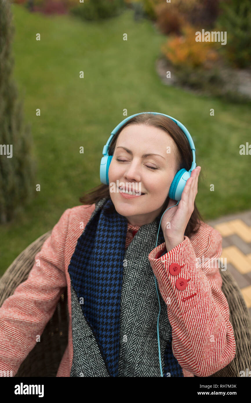 Heitere Frau zu Musik mit Kopfhörer außerhalb hören Stockfoto