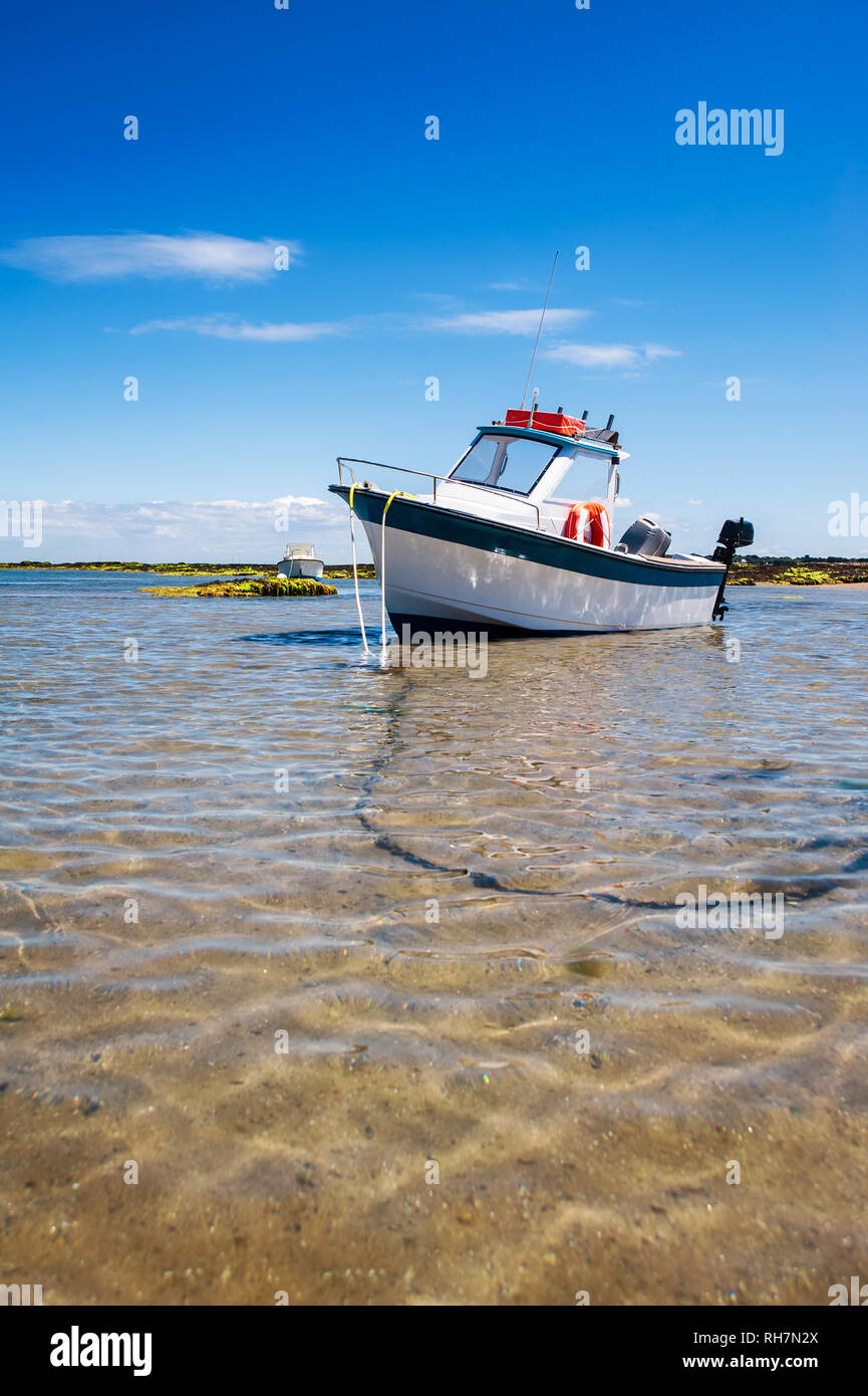 Weiße Boot auf Sand mit Wasser und Felsen im Sommer in Noirmoutier Stockfoto