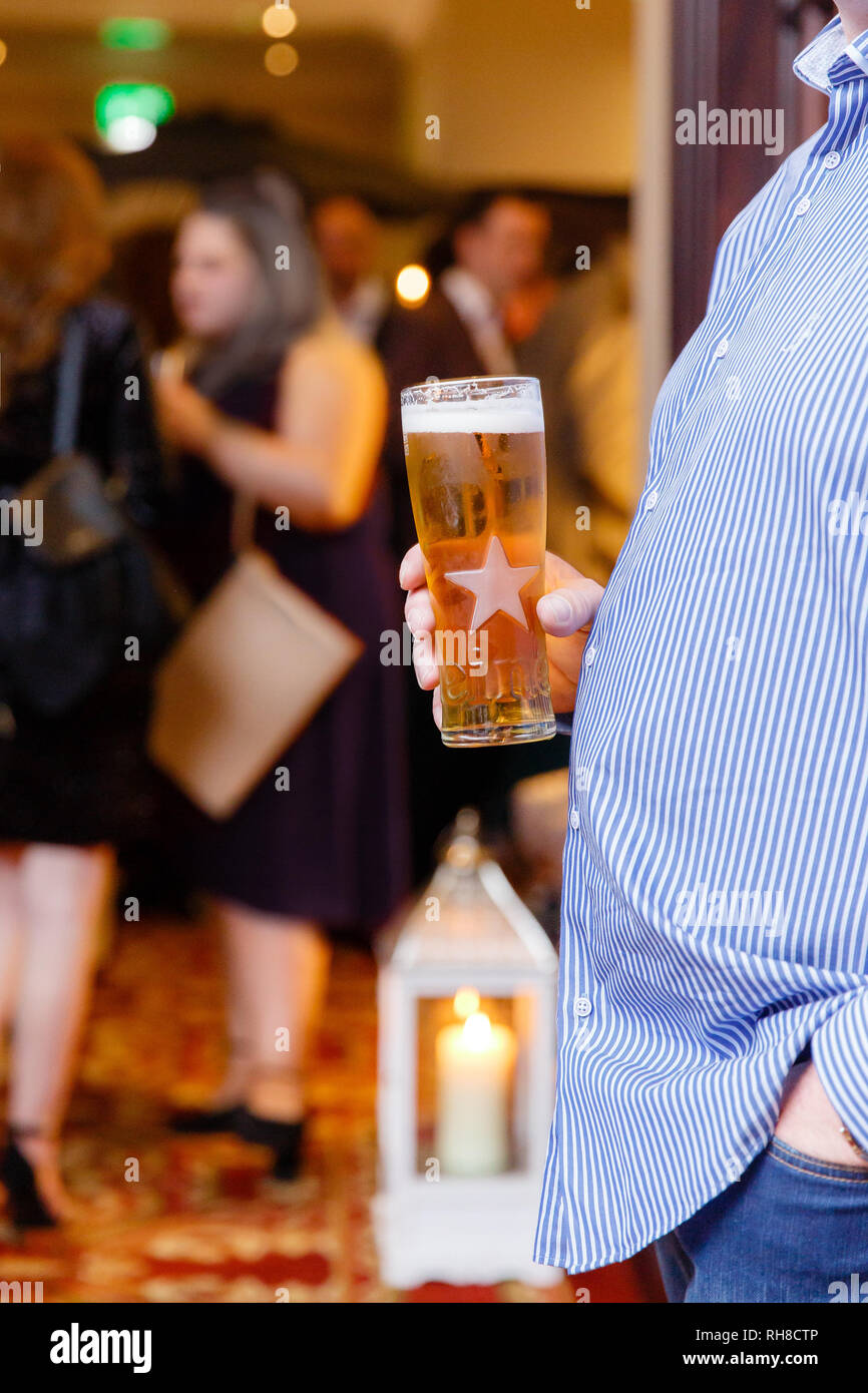 Mann mit Bierbauch mit einem Pint Bier in der Hand, die im Verlauf der Veranstaltung. Die Menschen in den Hintergrund. Stockfoto
