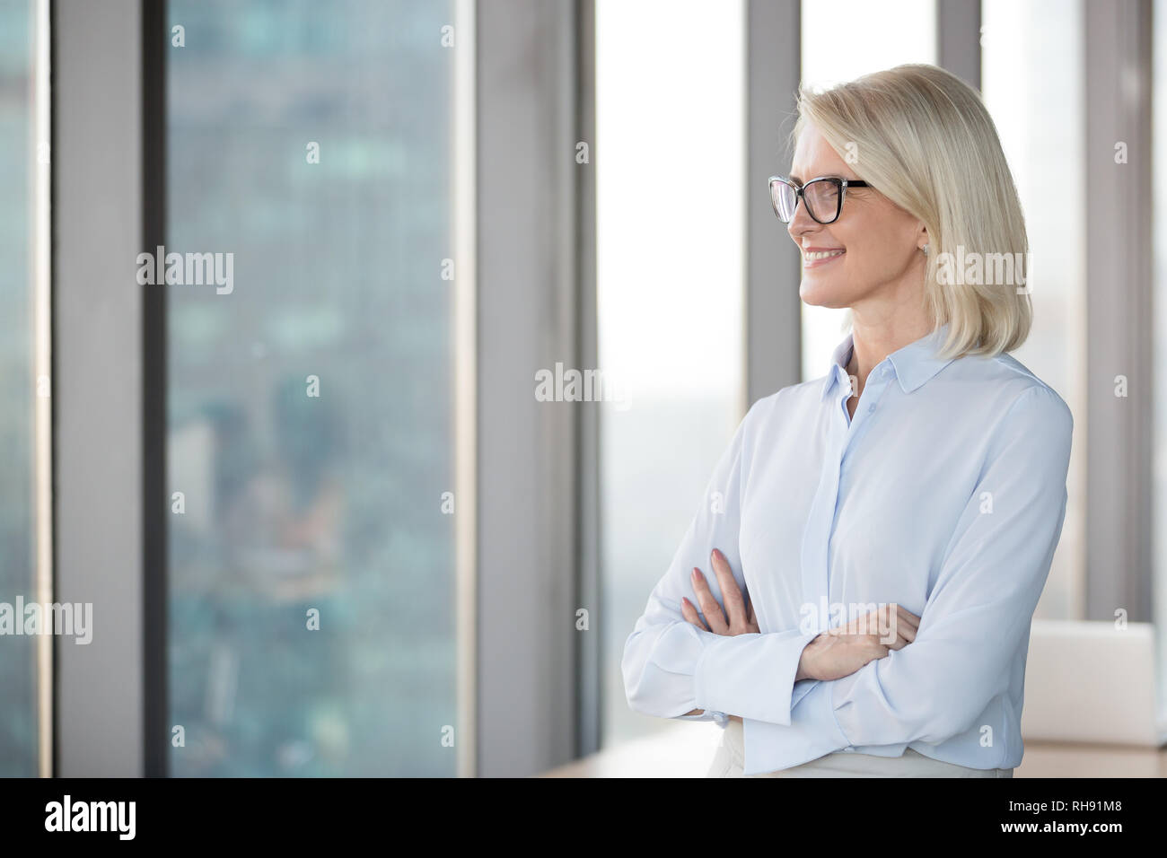 Lächelnd erfolgreiche Geschäftsfrau im mittleren Alter durch Fenster Stockfoto