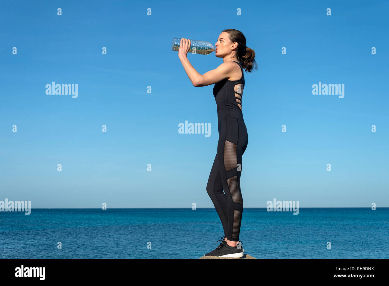 Sportlerin steht auf einem Felsen am Meer trinken aus einem Kunststoff Flasche Wasser Stockfoto