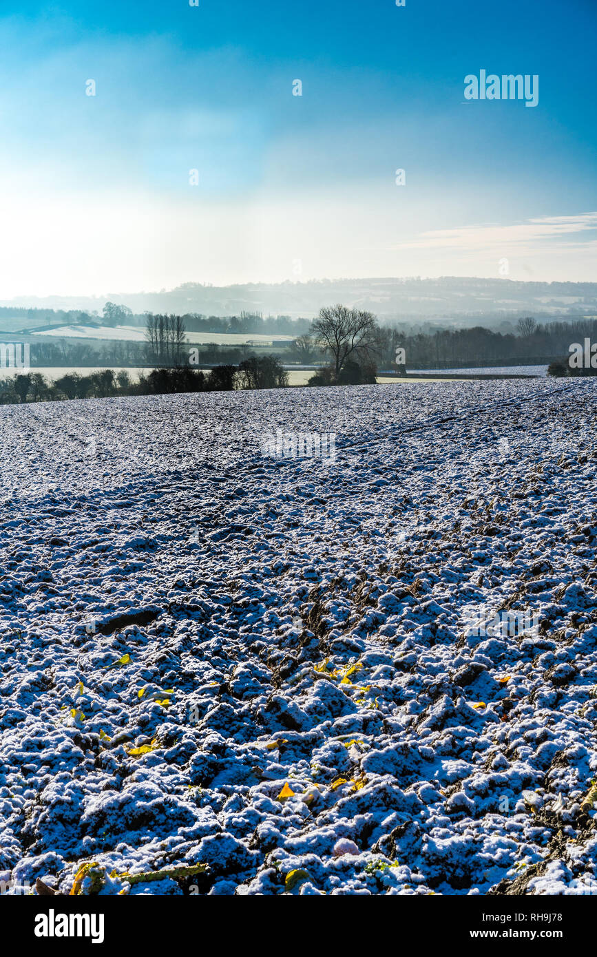Am frühen Morgen winter Aussicht, an einem sonnigen Tag über einen schneebedeckten gepflügten Feldes zu entfernten Misty Hills in den Cotswolds, Gloucestershire, VEREINIGTES KÖNIGREICH Stockfoto
