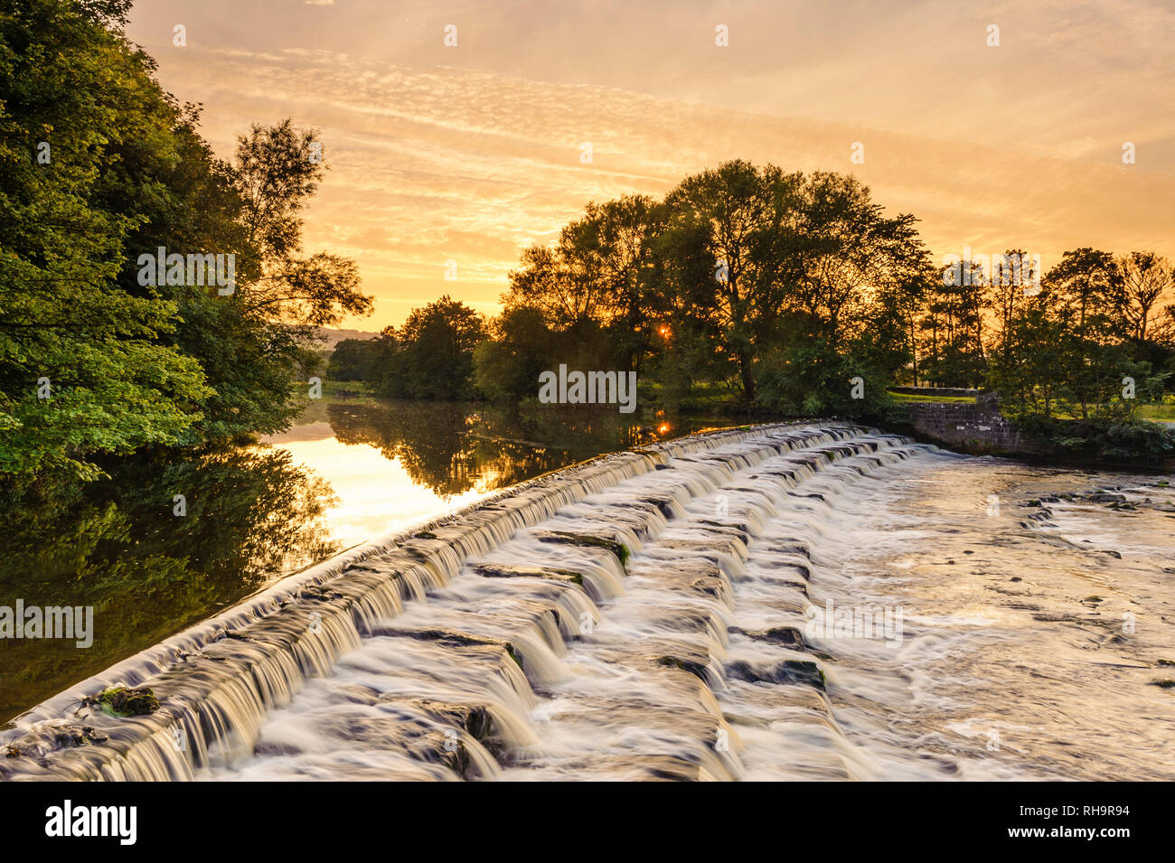 Einen malerischen Sonnenuntergang Himmel über ländliche Landschaft (Wasser sanft fließende Wehr Schritte) - River Wharfe, Burley in Bösingen, Yorkshire, England, UK. Stockfoto