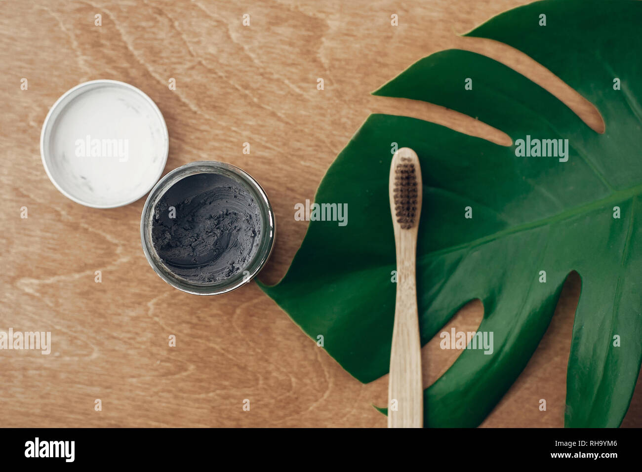 Natürliche Zahnpasta Aktivkohle in Glas und Bambus Zahnbürste auf Holz- Hintergrund mit grünen monstera Blatt. Kunststoff kostenlose Essentials, Zähne Stockfoto