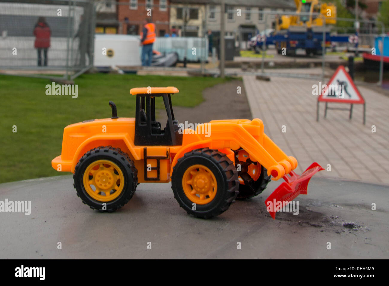 Lustiges Spielzeug Bulldozer mit echten Bau und Ausrüstung im Hintergrund Stockfoto