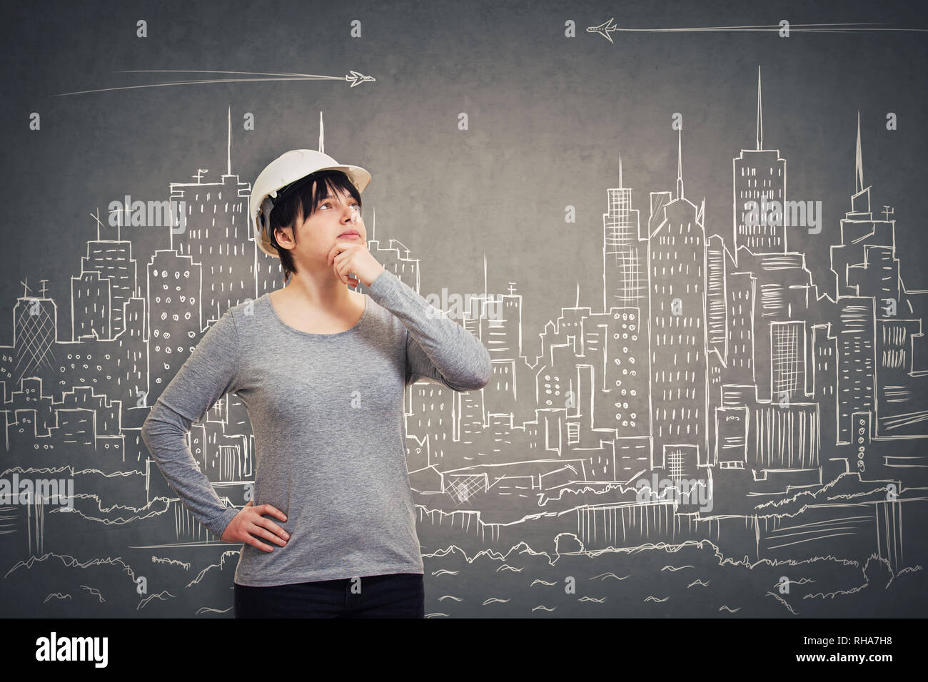 Geniale junge Frau Ingenieur das Tragen schützender helm die Hand unter dem Kinn, an neuen Ideen über eine imaginäre gezeichnet Stadt backgro Stockfoto