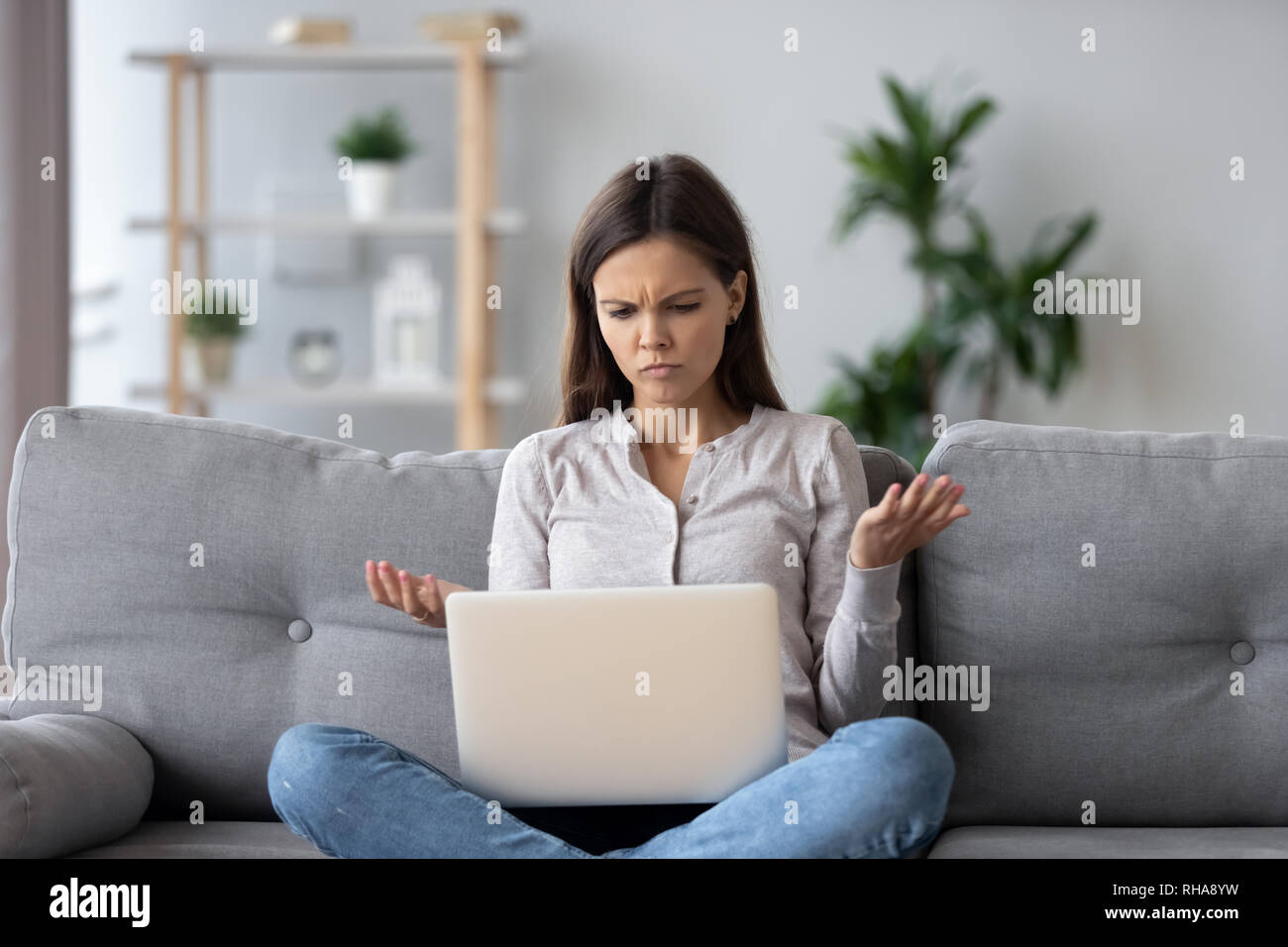 Verwirrte junge Frau auf der Suche nach Laptop fühlt sich durch Lesen online News verwirrt Stockfoto