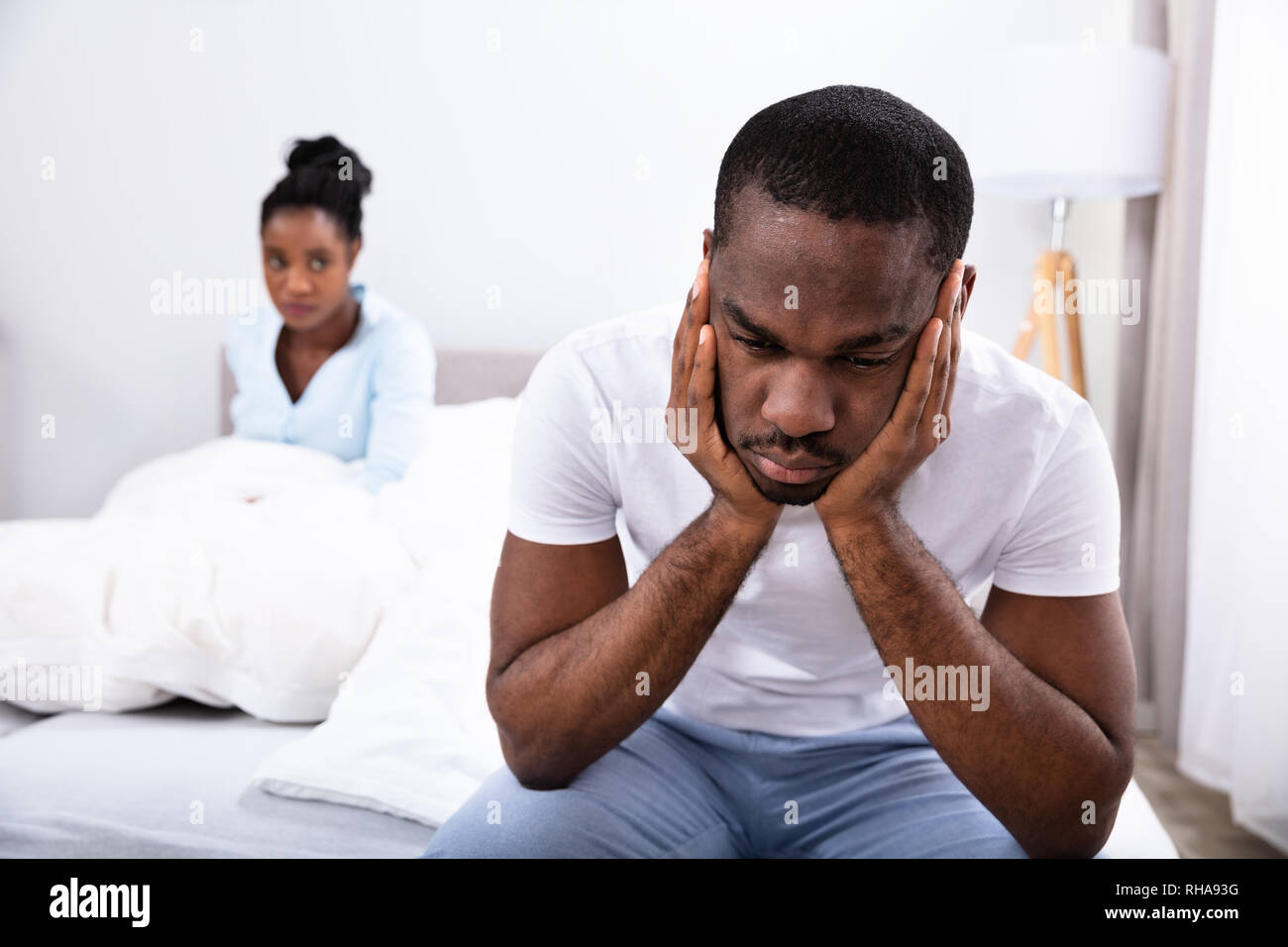 Verärgert jungen afrikanischen Mann sitzt auf dem Bett vor den Augen seiner Frau Stockfoto