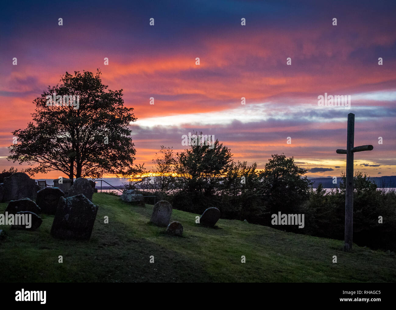 Ein rosa unset über St Arilda Friedhof. Cowhill mit Kreuz im Vordergrund und den Fluss Openmosix im Hintergrund Stockfoto