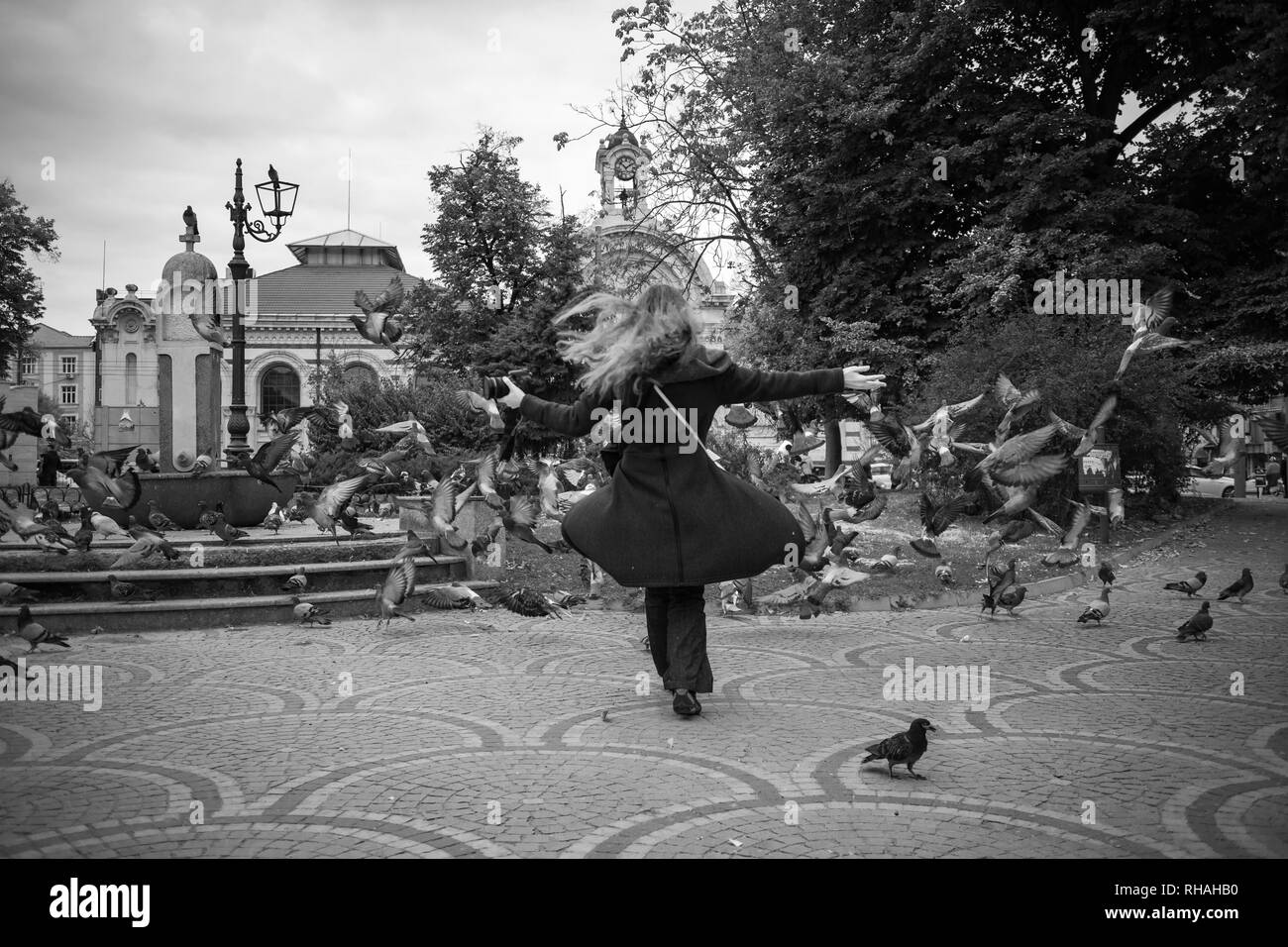 Schwarz-weiß Foto von schönen Mädchen, dass DSLR-Kamera wer spielt und jagen Herde von Tauben in Sofia in trüben Wintertag einen öffentlichen Ort sq Stockfoto