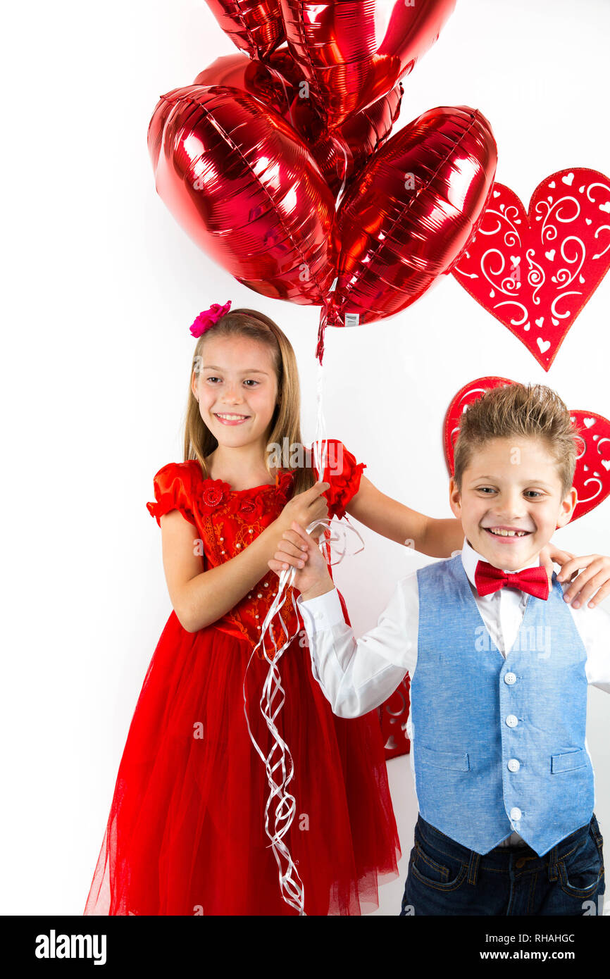 Saint Valentine's Day. Hübsches Mädchen mit roten Kleid und Gentleman Boy mit blauer Weste, Red Butterfly Krawatte, rote Rosen Schaufel und Herzförmigen Geschenkbox. Va Stockfoto