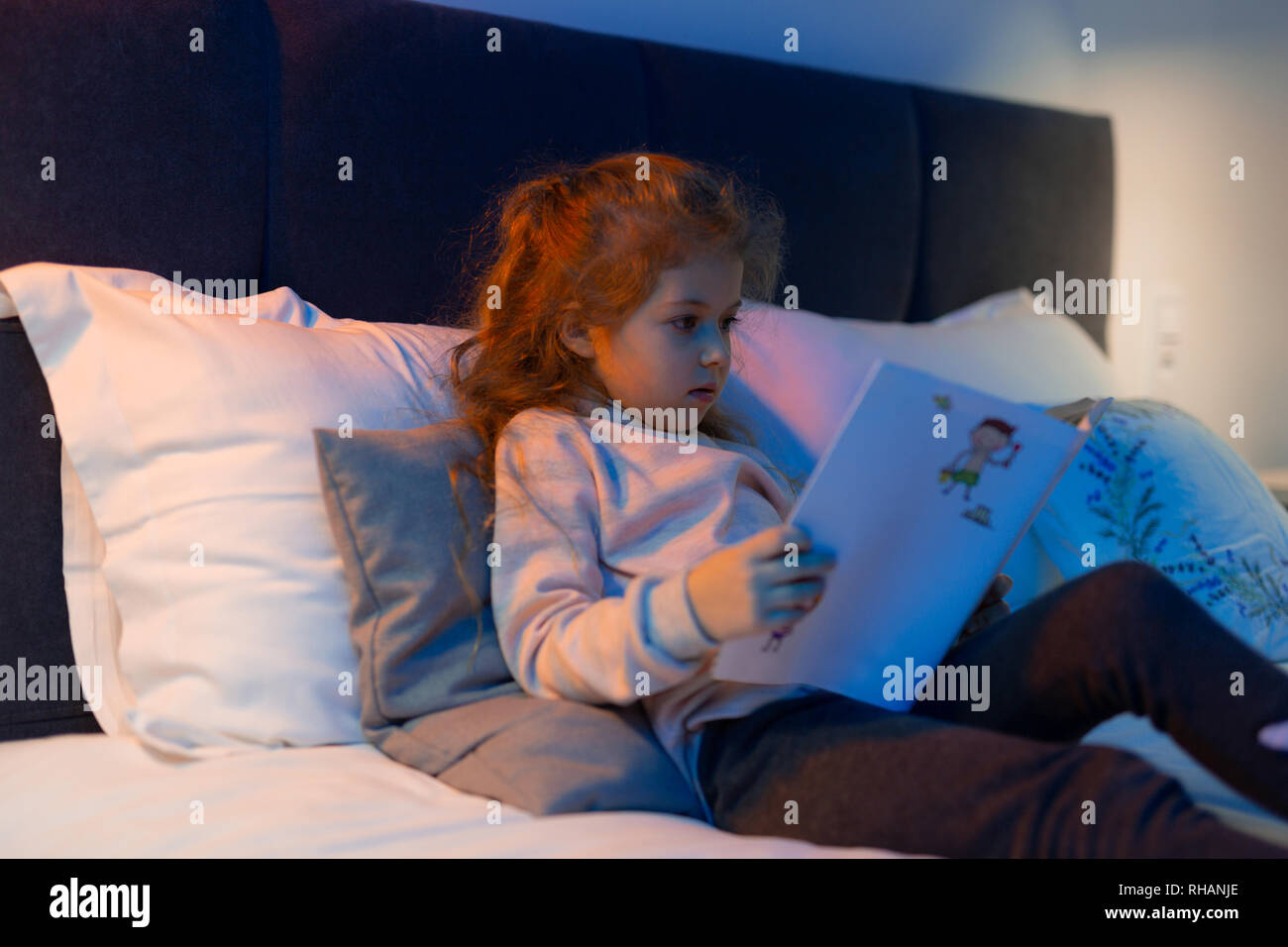 Kleines süßes langhaarige Mädchen mit einem Buch im Bett Stockfoto