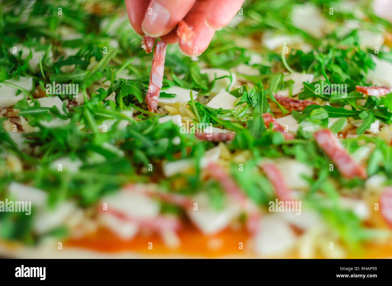 Der Pizza. Italienische Salami Pizza mit Champignons, Rucola, Tomaten, Mozzarella, Knoblauch und Soße. Koch fügt Zutaten für Pizza Stockfoto
