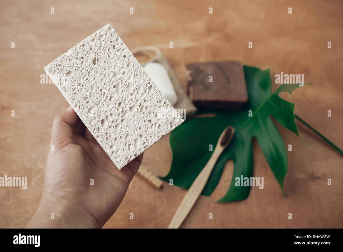 Hand, die natürlichen Ökosysteme schwamm auf dem Hintergrund von Bambus Zahnbürste, Seife, Shampoo, crystal Deodorant, auf Holz mit grünen monstera Blatt. Null war Stockfoto