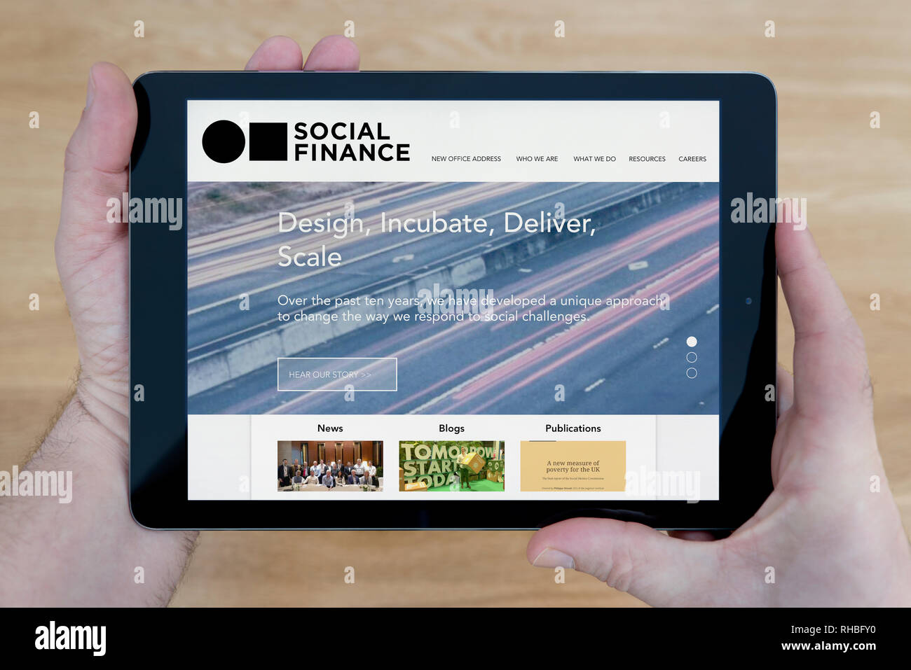 Ein Mann schaut auf die Social Finance Website auf seinem iPad tablet device, Schuß gegen einen hölzernen Tisch top Hintergrund (nur redaktionelle Nutzung). Stockfoto
