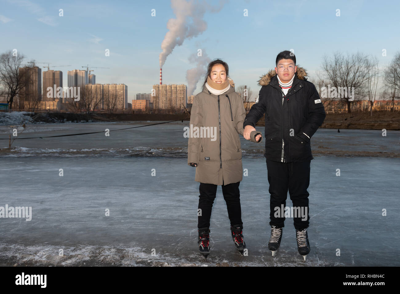 Junges Paar auf Skates, halten sich an den Händen an eine Eisbahn am Ufer der SongHua Fluss, Jilin Stadt Stockfoto