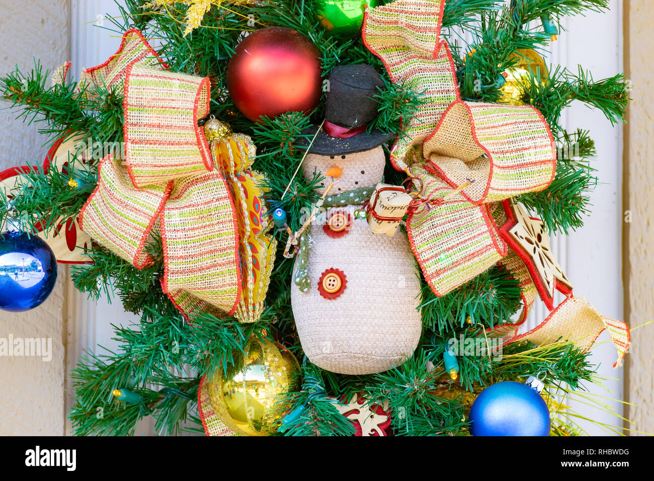 Weihnachten Winter Dezember Urlaub Dekor. Tür Kranz mit bunten Bändern, glänzendes Metall dekorative Kugeln und einen Schneemann Teddybär. Stockfoto