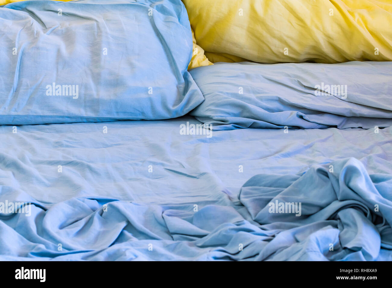 Unordentliche ungemachten Bett mit blauen und gelben und blauen Kissen Stockfoto