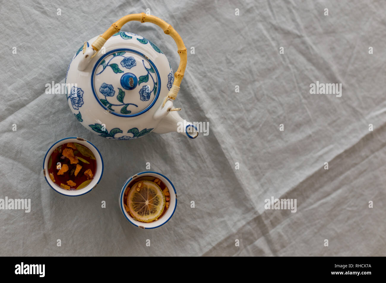 Obere Ansicht geschossen von Kräuter Tee mit Zitrone in whtie und blau Keramik Tasse und Kännchen serviert auf grau Leinen Tischdecke. Horizontale geschossen und negativen Raum. Stockfoto