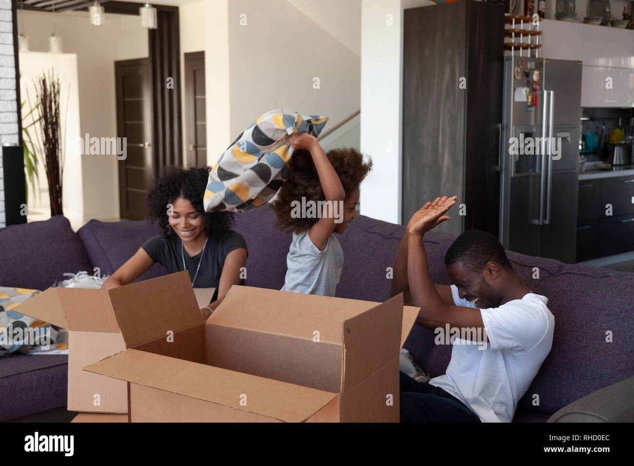 Glückliches Kind in Afrika genießen Kissenschlacht mit Eltern, die Kisten packen Stockfoto