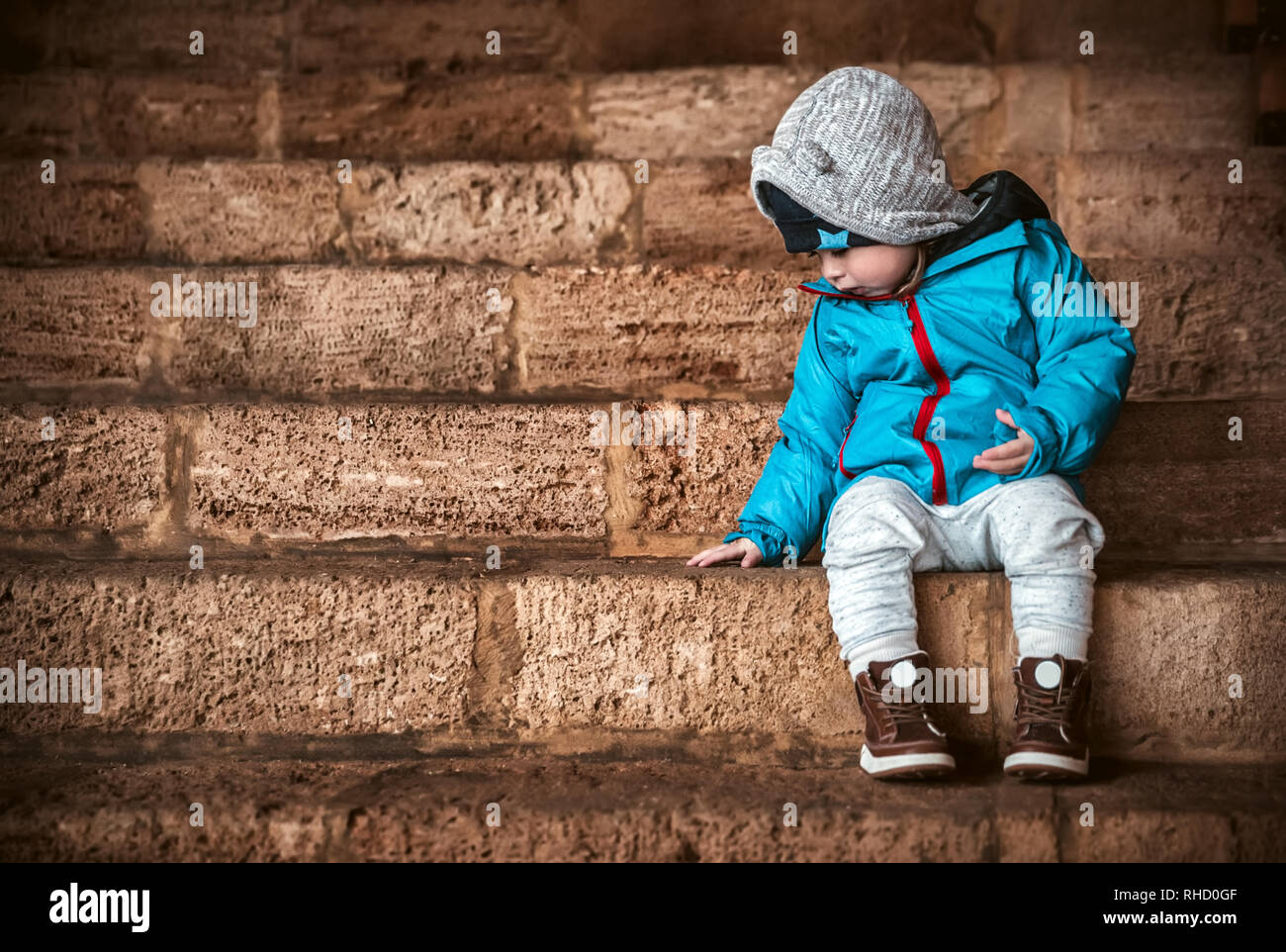 Süße kleine Baby boy in warme Kleidung sitzt auf der Treppe und wartet auf einen Eltern im Hof spazieren zu gehen gekleidet, glückliche unbeschwerte Kindheit Stockfoto