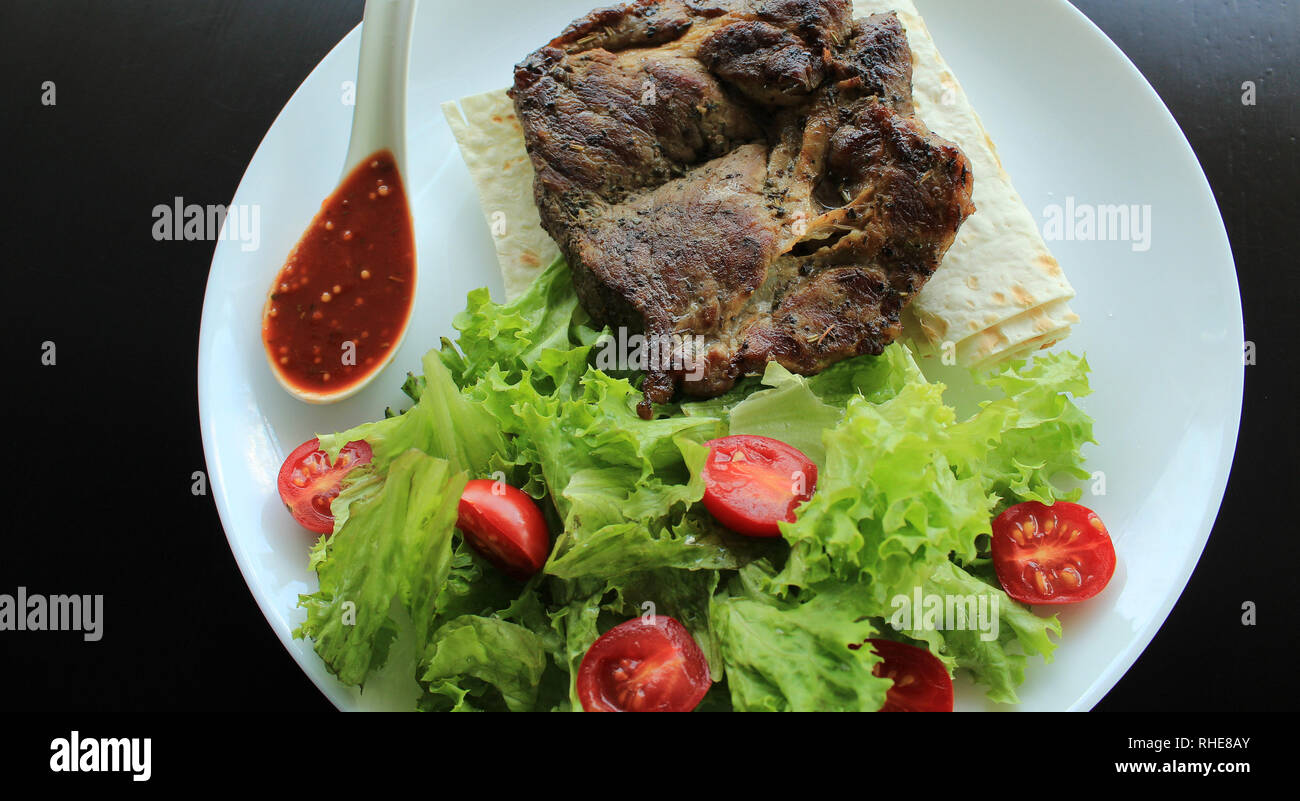 Gegrilltes Rumpsteak serviert mit Tomaten, Salat, Hot Sauce und dünne Fladenbrot Stockfoto