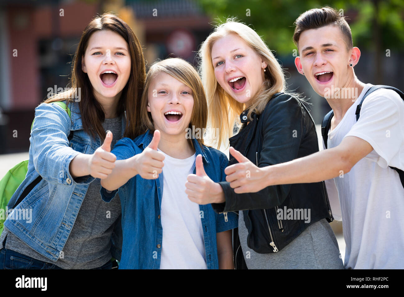 Portrait von vier fröhlichen Jugendlichen stehen und halten die Daumen zusammen im Freien Stockfoto