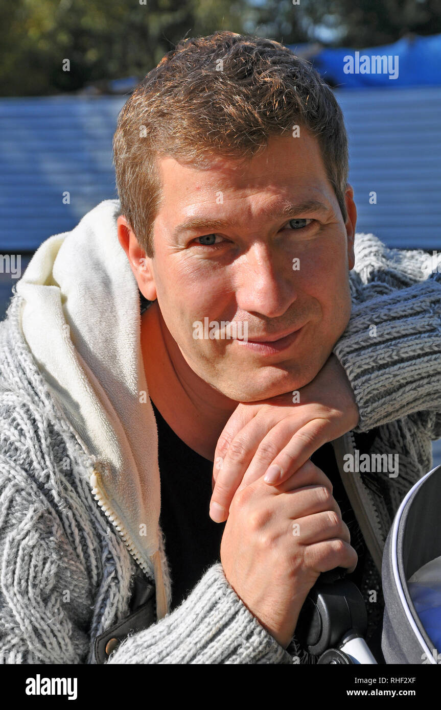 Porträt eines lächelnden kaukasischen Mann in grauen pullover mit verschränkten Armen im sonnigen Tag Stockfoto