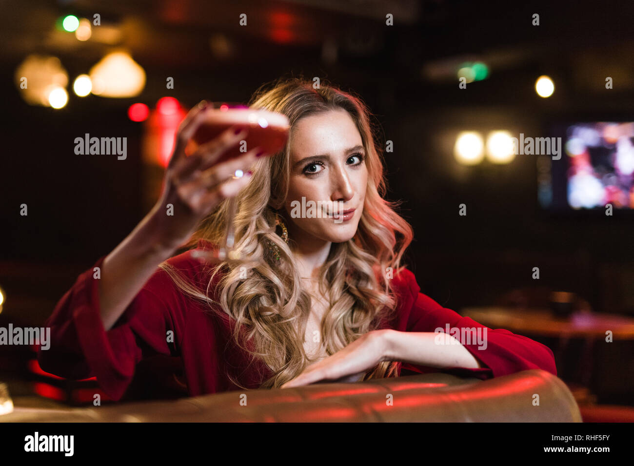 Eine fröhliche junge blonde Frau in einer Bar, die eine rosa Cocktail Stockfoto