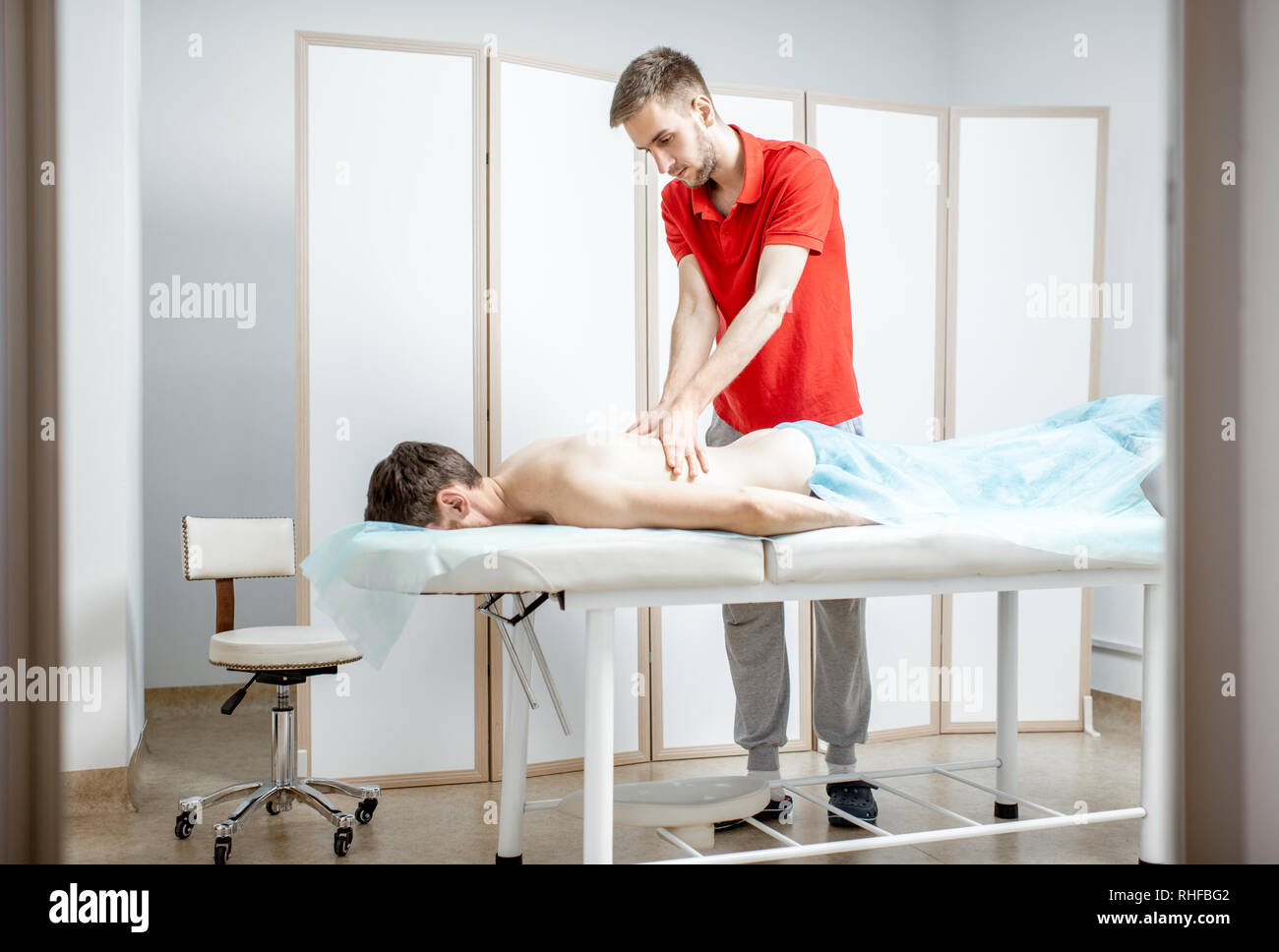 Junge männliche Therapeuten, Rückenmassage, die einem Mann im weißen Schrank der Rehabilitationsklinik liegen Stockfoto