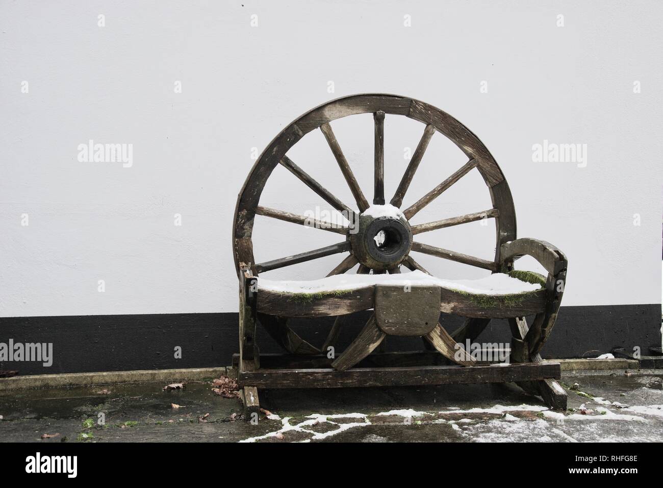 Eine natürliche Holz- dem Sitz oder der Sitzbank für den Garten, die aus einem Wagen oder Mühlrad. Es ist leicht in Schnee und gegen eine weiße Wand die Pa abgedeckt Stockfoto