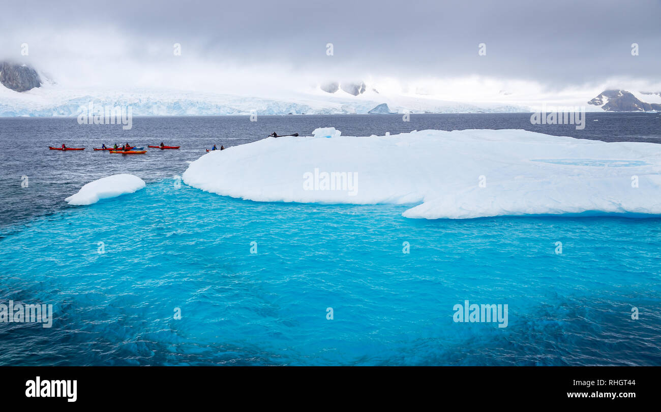 Riesiger Eisberg mit blauen Unterwasser teil und kleinen Touristen Kajaks mit Antarktis Lagune im Hintergrund, Peterman Island, Antarktische Halbinsel Stockfoto