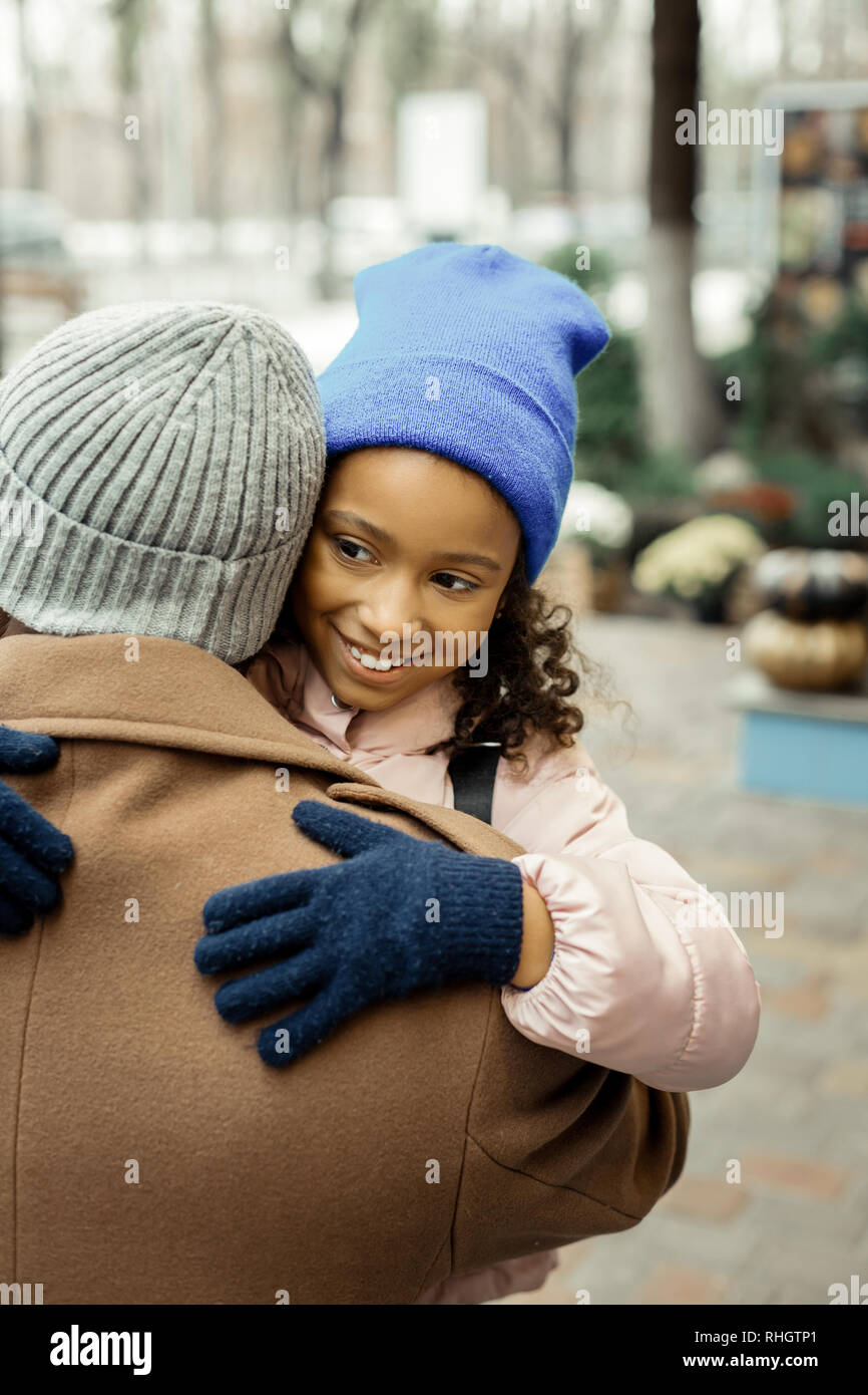 Vaters Mantel tragen, Beige und Grau hat seine jüngere Tochter umarmen Stockfoto