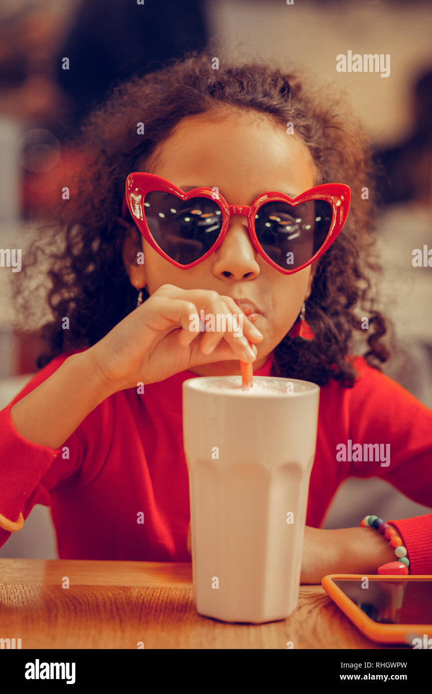 Lustige süße Mädchen tragen rote Sonnenbrille trinken Milchshake Stockfoto