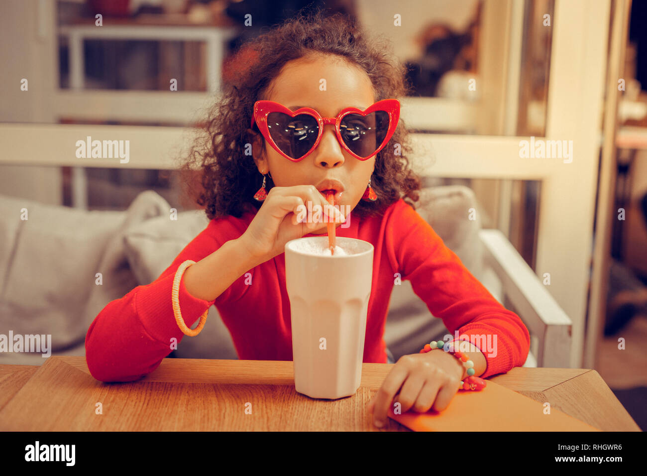 Stilvolle Mädchen tragen rote Rollkragen und Sonnenbrille in der Cafeteria sitzen Stockfoto