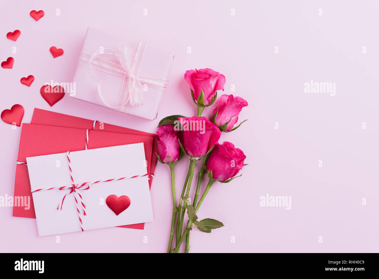 Valentines Tag und liebe Konzept. Rosa Rosen, Geschenkbox mit roten Herzen und rot rosa Anschreiben auf rosa Hintergrund. Stockfoto