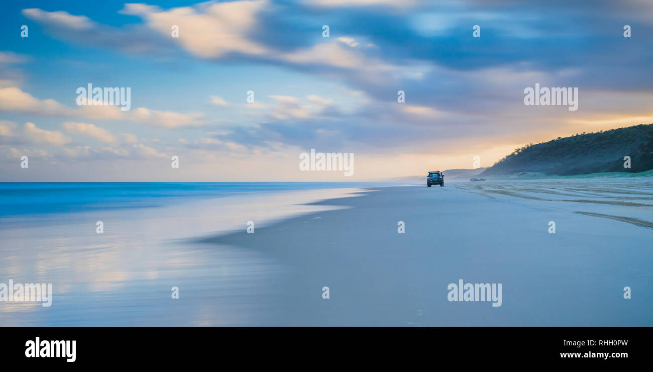 Auto fahren auf einer menschenleeren Strand im Süden der Insel bei Sonnenuntergang in Queensland, Australien Stockfoto