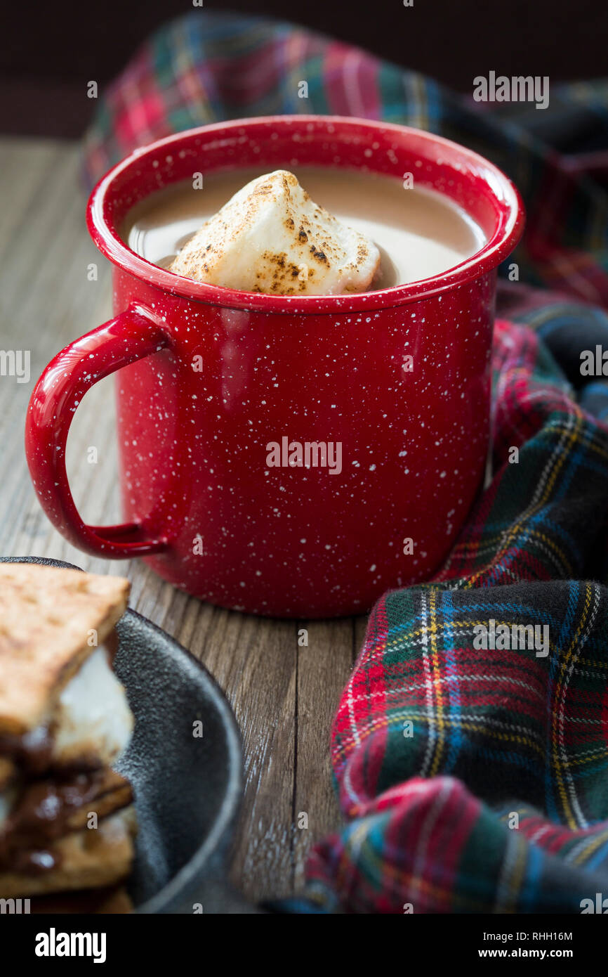 Tasse heiße Schokolade mit gerösteten Marshmallows in Rot gesprenkelt enamelware Becher mit plaid Decke und ein Smores-kit Stockfoto