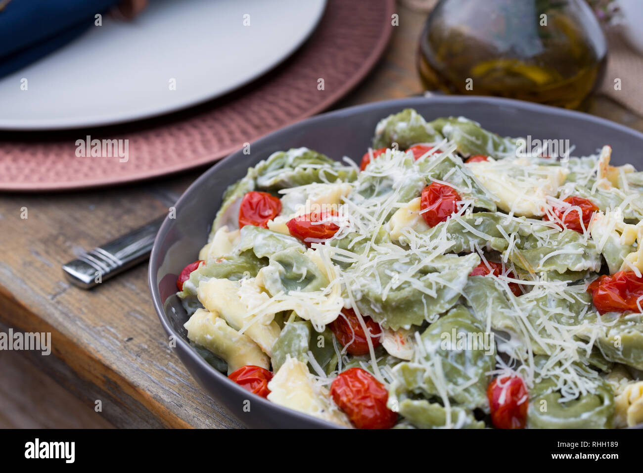Servierschale von Grün und Gelb Ravioli mit Tomaten und geriebenem Parmesan auf hölzernen Tisch für Hinterhof outdoor Dinner Party. Stockfoto