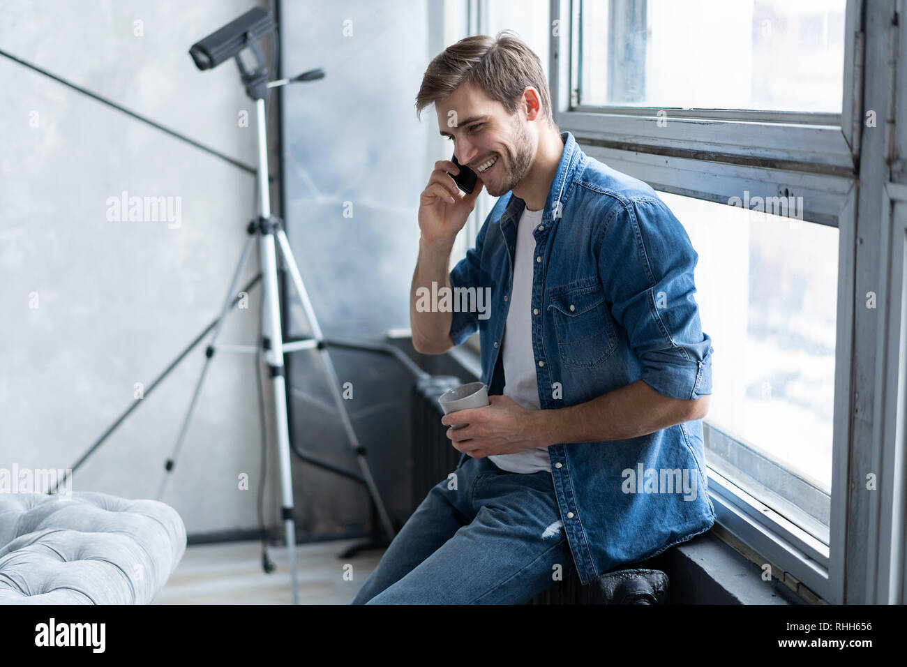 Lächelnden jungen Mann Gespräch am Handy, am Fenster zu Hause suchen. Stockfoto