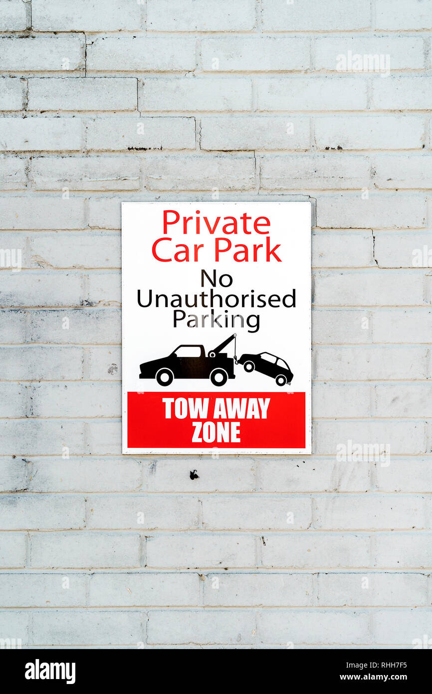 Privater Parkplatz Schild mit Grafik der einen Abschleppwagen ein Auto abschleppen und Text Beratung keine unbefugten Parken auf einer weißen Wand montiert Stockfoto